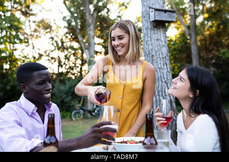 Host pouring wine into glasses at a summer dinner in the garden Stock Photo