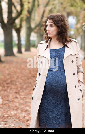 Portrait of pregnant woman wearing trenchcoat and blue dress in autumn