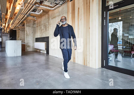 Mature businessman on cell phone walking in modern office Stock Photo