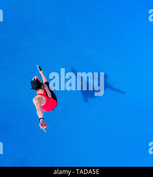 Jumping young woman and her shadow on blue background, top view Stock Photo