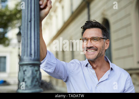 Portrait of happy businessman leaning against lamp post in the city Stock Photo