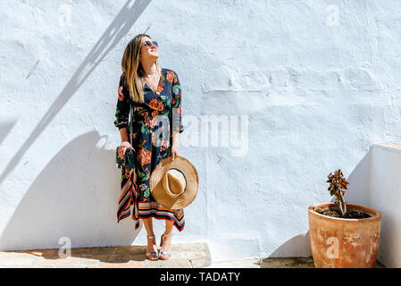 Spain, Cadiz, Vejer de la Frontera, fashionable woman standing in front of white wall looking up Stock Photo