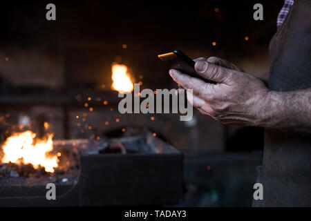 Close-up of blacksmith holding cell phone in his workshop Stock Photo