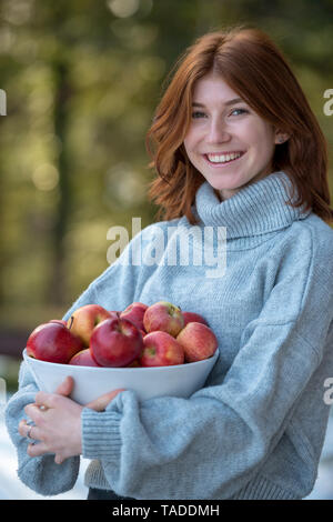 Portrait of redheaded teenage girl holding bowl of apples Stock Photo