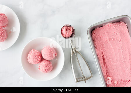 Homemade pink forced rhubarb ice cream in stainless steel tub, ice cream scoop and on plates. Top view. Stock Photo