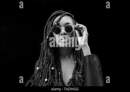 Portrait of woman with dreadlocks wearing sunglasses in front of black background Stock Photo