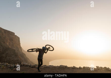Spain, Lanzarote, mountainbiker on a trip at the coast at sunset carrying his bike Stock Photo