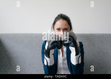 Portrait of young woman on couch wearing boxing gloves Stock Photo