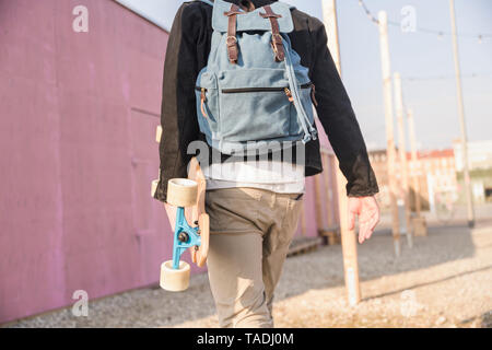 Rear view of young man with skatebaord and backpack on the move in the city Stock Photo