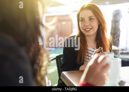 Portrait of redheaded young woman with nose piercing looking at her friend at pavement cafe Stock Photo
