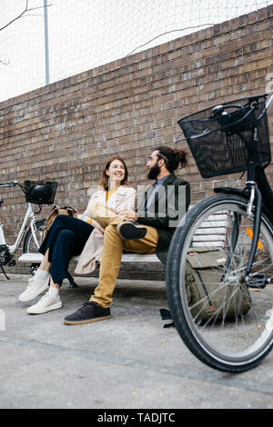 Couple sitting on a bench next to e-bikes talking Stock Photo