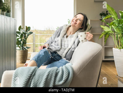 Happy woman with a mug and tablet sitting on the couch at home Stock Photo