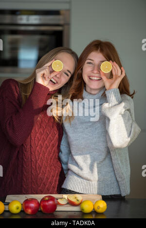 Two laughing friends holding lemon halves in front of their eyes Stock Photo
