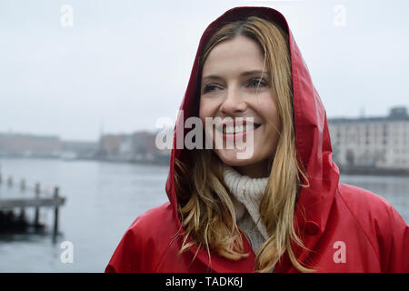 Denmark, Copenhagen, portrait of happy woman at the waterfront in rainy weather Stock Photo