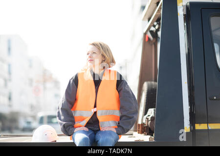 Woman wearing reflective vest sitting on truck platform Stock Photo