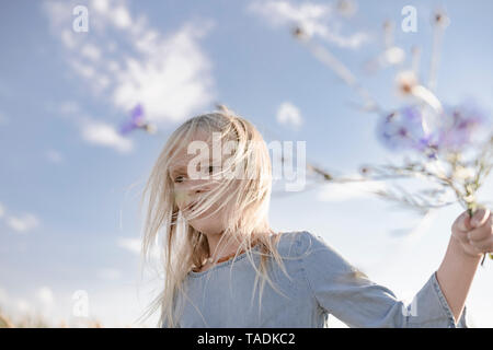 Blond girl with windswept hair holding cornflowers Stock Photo
