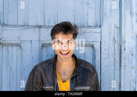 Portrait of laughing man in front of lightblue wooden door Stock Photo