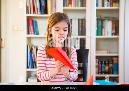 Girl tinkering paper plane on table at home Stock Photo