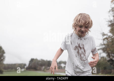 Portrait of blond boy with dirty face and t-shirt after jumping into a puddle Stock Photo