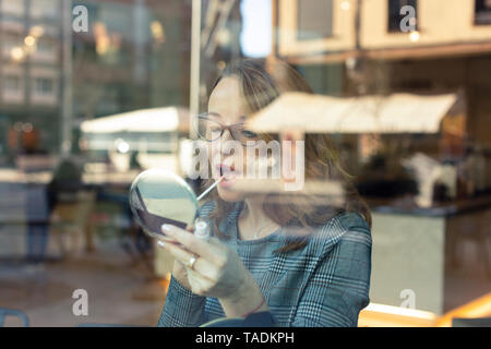 Mature woman with beauty mirror applying make-up in a cafe Stock Photo