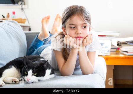 Portrait of little girl lying on couch with cat