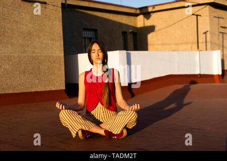 Teenage girl meditating on roof terrace at sunset Stock Photo