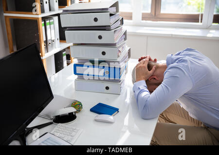 Stressed Businessman Looking Down Near Folders While Working At Desk Stock Photo