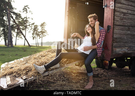 Happy young couple sitting on trailer in the countryside Stock Photo