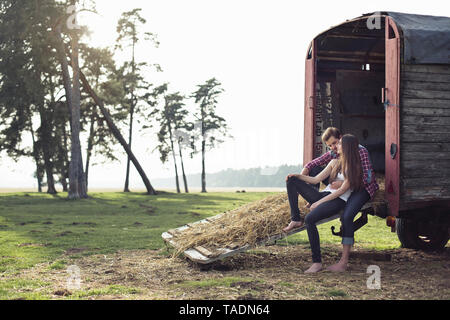 Happy young couple sitting on trailer in the countryside Stock Photo