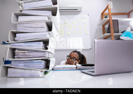 Close-up Of Businesswoman Hiding Behind The Desk With Stack Of Folders And Laptop Stock Photo