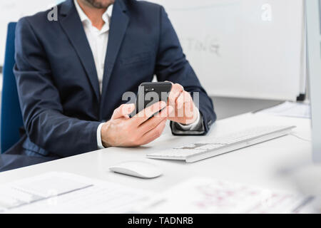 Close-up of businessman sitting at desk in office using cell phone Stock Photo