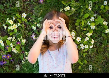 Girl looking through fingers, lying on flower meadow, top view Stock Photo