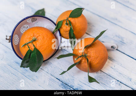 Three oranges with leaves and a colander on wood Stock Photo