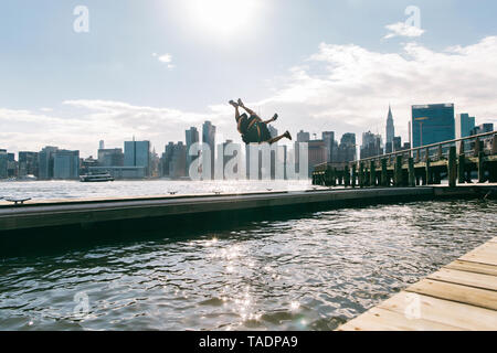 USA, New York, Brooklyn, two young men doing backflip on pier in front of Manhattan skyline Stock Photo
