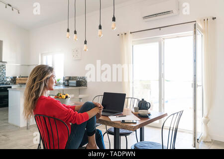 Woman using laptop on dining table in modern home Stock Photo