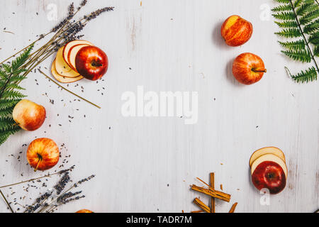 Sliced and whole apples, fern leaves, cinnamon sticks and lavender on white wood Stock Photo
