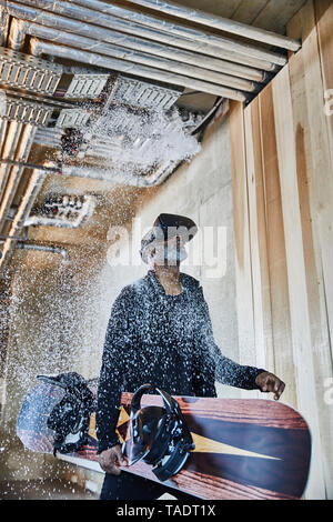 Mature businessman wearing VR glasses holding snowboard in office with splashing snow Stock Photo