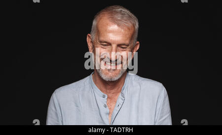 Close up of a laughing senior man against black background. Portrait of smiling senior man looking down. Stock Photo