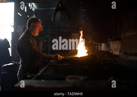 Blacksmith working at forge in his workshop Stock Photo