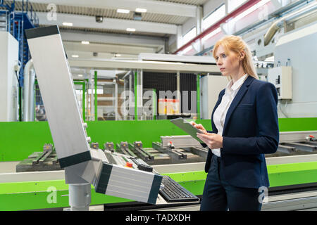 Businesswoman using tablet at machine in factory Stock Photo