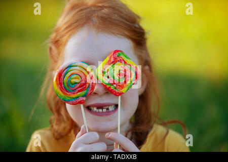 Happy girl covering her eyes with lollipops Stock Photo