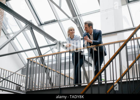 Businessman and woman standing in office building, discussing Stock Photo
