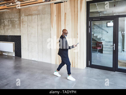 Mature businessman with cell phone walking in modern office