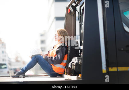 Woman wearing reflective vest sitting on truck platform Stock Photo