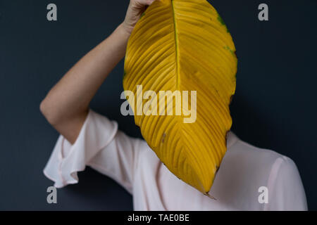 Woman covering face with a yellow banana leaf Stock Photo