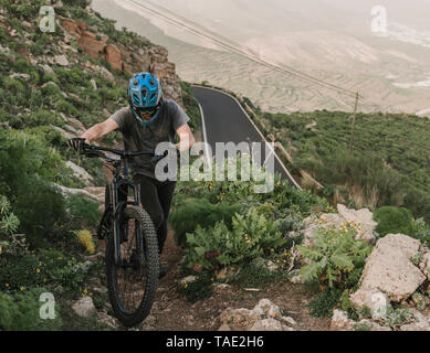 Spain, Lanzarote, mountainbiker pushing his bike on a trail in the mountains Stock Photo