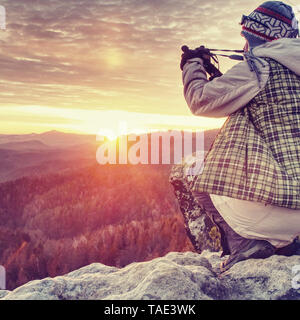 Photographer taking picture. Woman artist photo enthusiast stay with camera above valley and works. Nice view over dried trees in valley. Stock Photo