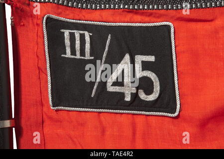 An SS Sturm flag of III./45 in Rosenberg/Upper Silesia complete with pole and finial Red flag cloth with black-silver fringe on three sides, both sides with a stitched-in white disc and a slanted swastika with black surfaces trimmed in silver cord. Silver embroidered 'III/45' for the 3rd Sturmbann (Rosenberg O.S) of 45th SS Foot Standarte (Neisse O.S.). Seven directly stitched-on nickel-plated standard rings. Supply stamping, small blemishes. Dimensions ca. 120 x 145 cm. Two-piece black wooden flagstaff. Nickel-plated finial in the form of a lance tip, punched 'RZM M3/39/40, Editorial-Use-Only Stock Photo