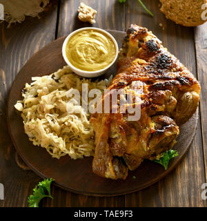 Roasted pork knuckle (eisbein) with braised cabbage (sauerkraut) and mustard on wooden table Stock Photo