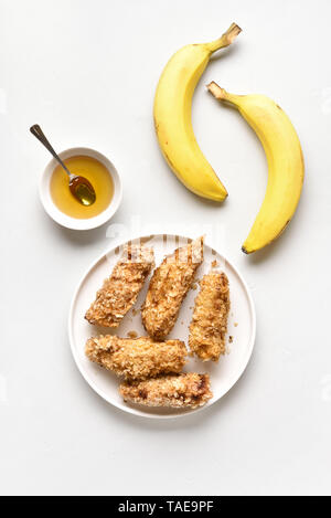 Tasty deep fried bananas on plate over white stone background. Dessert from pan fried bananas in asian style. Top view, flat lay Stock Photo